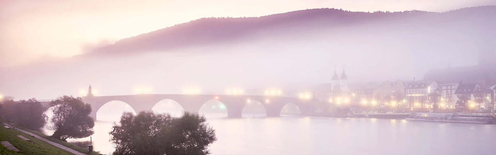 Reportagefotografie: Die Alte Brücke in Heidelberg im Morgennebel über einem Fluss.